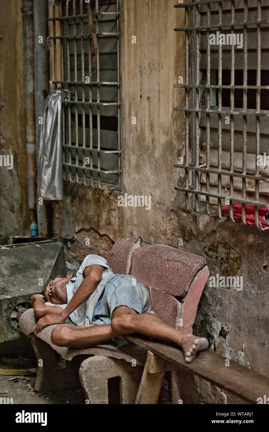 Homeless man sleeps in a bench of a tenement`s alley Stock Photo